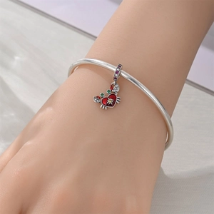 Close-up of silver bracelet with red enamel crab heart charm and glowing gemstones