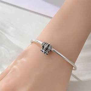 Close-up of silver crown charm with blue enamel and crystals on a sleek bangle