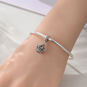 Detail shot of crown charm with red stones and vintage silver bracelet on wrist