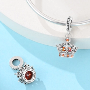 Detail of silver crown charm with orange gemstones and 'be your own queen' engraving