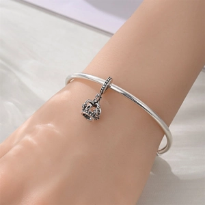 Detail of silver crown charm pendant on an open bangle bracelet worn on wrist
