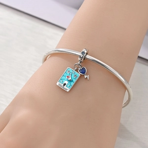 Detail of silver Judgement tarot card charm and blue heart bolt charm on a bracelet