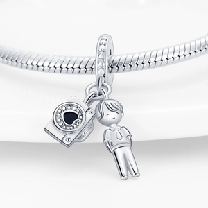 Macro detail of silver camera and smiling boy charms on a snake chain bracelet