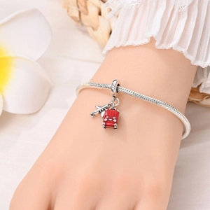Travel themed silver charm bracelet featuring airplane and red suitcase charms on wrist