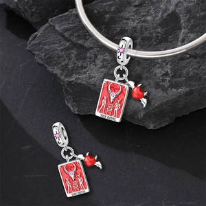 Macro detail of silver Tarot Devil charm with red enamel and pink crystal accents