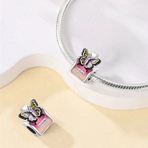 Detailed view of pink perfume bottle charm with butterfly motif on silver bracelet