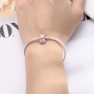 Close-up of pink enamel car charm on a silver snake chain bracelet worn on a wrist