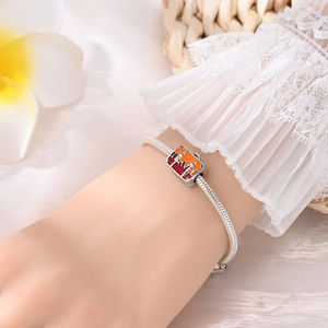 Silver snake chain bracelet with a colorful travel suitcase charm on a lace sleeve wrist