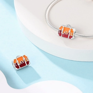 Detailed view of silver travel suitcase charm with orange enamel and TRAVEL engraving