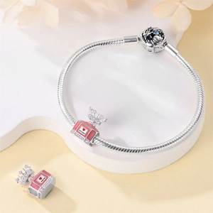 Detail of pink perfume bottle pendant and crown bead on silver snake chain bracelet