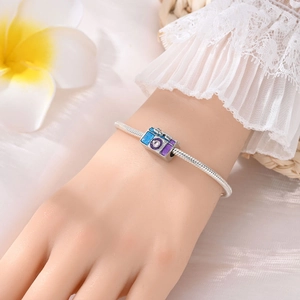 Detailed view of a silver camera charm with purple enamel and zircon on a snake chain