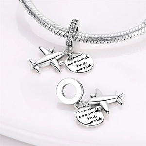 Macro detail of silver airplane charm and engraved travel pendant with zircons