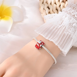 Detail of silver snake chain bracelet featuring a red enamel car charm on a wrist