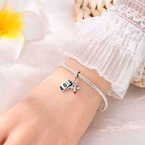 Detail of travel charm bracelet featuring a blue passport and silver airplane pendant