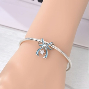 Silver open bangle featuring a blue enamel bow with zircon and hollow star charm