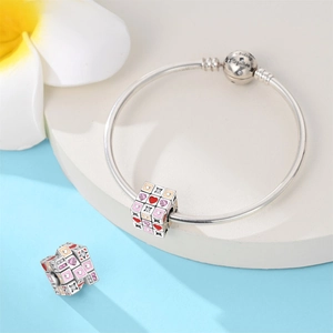 Vista de detalle de pulsera de plata con dije de cubo grabado y esmalte de corazón rosa