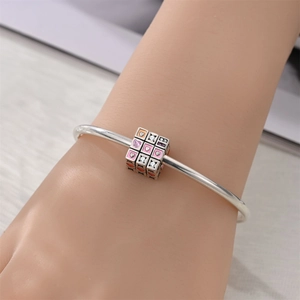 Detalle de brazalete de plata con dijes de cubo de corazón y cristales rosas en la muñeca