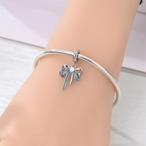 Detalle de pulsera plateada con colgante de mariposa esmaltada azul y perla en la muñeca