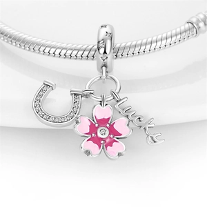 Macro shot of silver horseshoe, pink enamel cherry blossom, and lucky charms on snake chain