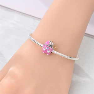 Detalle de brazalete plateado con amuleto de carroza en esmalte rosa y cristales azules