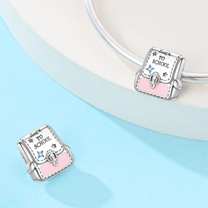 Macro detail of silver backpack charm with pink enamel and Back to School engraving