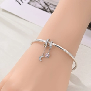 Primer plano de brazalete plateado con dijes de luna, estrella y flor de circón rosa