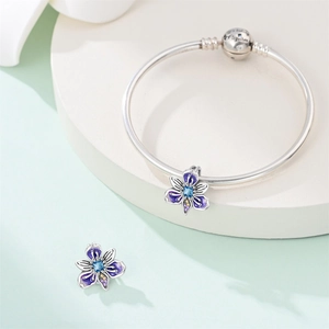 Detail of silver iris charm bracelet with purple enamel petals and blue crystal heart