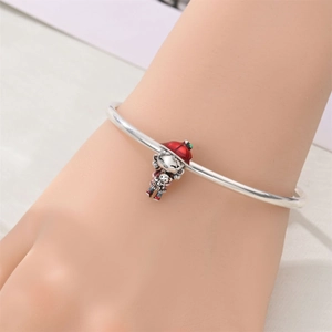 Primer plano de una pulsera plateada con un lindo colgante de niña en esmalte de color rojo