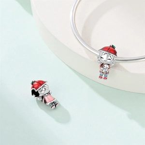 Vista detallada de un dije de niña plateado con gorro rojo y oso blanco en pulsera