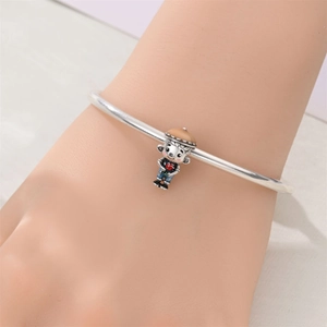 Detalle de dije de pulsera plateado con niño en overol azul y decoración de corazón rojo