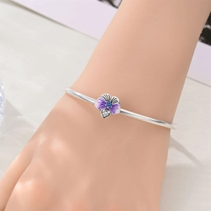 Detail of silver iris charm bracelet with purple enamel petals and blue crystal center