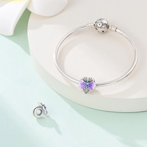 Macro shot of silver bangle with purple enamel pansy charm and sparkling blue gemstone