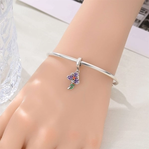 Silver bangle with purple enamel pansy flower charm on woman's wrist in soft light