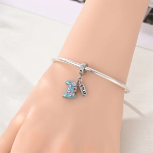 Detalle de brazalete plateado con amuleto de mando azul claro y placa PLAY en la muñeca