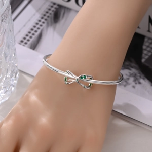 Detailopname van zilveren oneindigheidsknoop armband met groene zirkoon om een vrouwenpols