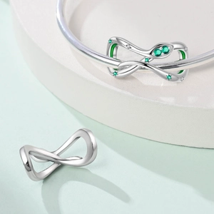 Detail van zilveren infinity bedeltje met groene edelstenen en zirkoon voor armband