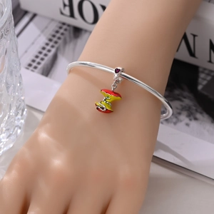 Detail van een zilveren armband met appel en slang hanger en hartvormige edelsteen