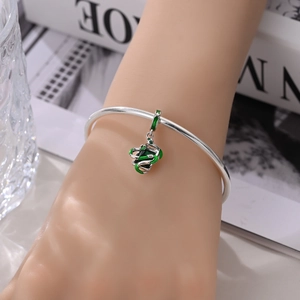 Detail van een zilveren slangenbedel met groen email op een metalen bangle armband
