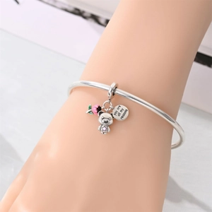 Dettaglio di bracciale in argento con fiore in smalto rosa, ciondolo orso e targa incisa
