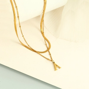 Détail d'un collier double rang doré avec chaîne serpent et pendentif lettre A chic