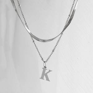Détail d'un collier argenté à deux rangs avec chaîne serpent et pendentif lettre K