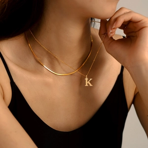 Détail d'un collier multicouche doré en acier inoxydable avec chaîne serpent et pendentif K