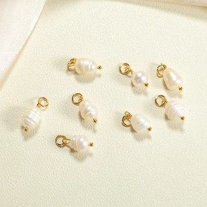 Macro view of natural baroque pearl charms with gold closed rings on silk fabric