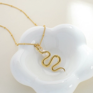 Golden snake pendant necklace with a freshwater pearl in a white porcelain dish