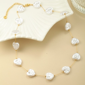 Detalle de collar dorado con perlas de corazón blancas y cierre sobre plato de concha