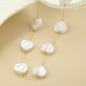 Detalle de collar dorado con perlas blancas en forma de corazón sobre cuero beige