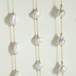 Primer plano de dijes de luna, concha y perlas de agua dulce en delicados collares dorados