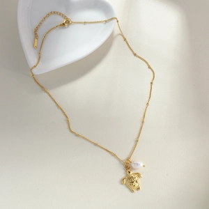 Dettaglio della collana con ciondolo a tartaruga dorata e perla su piatto