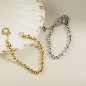 Détail de bracelets à perles dorés et argentés avec fermoirs mousquetons sur un coquillage