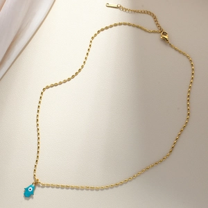 Macro view of gold Hamsa Hand pendant with blue enamel Evil Eye on beaded chain